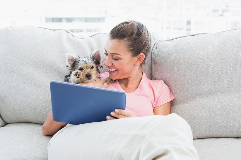 Cheerful woman using tablet with her yorkshire terrier at home i